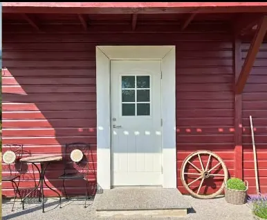 Valge uks punases laudmajas, kõrval väike laud kahe tooliga ja vana vankriratas seina najal.